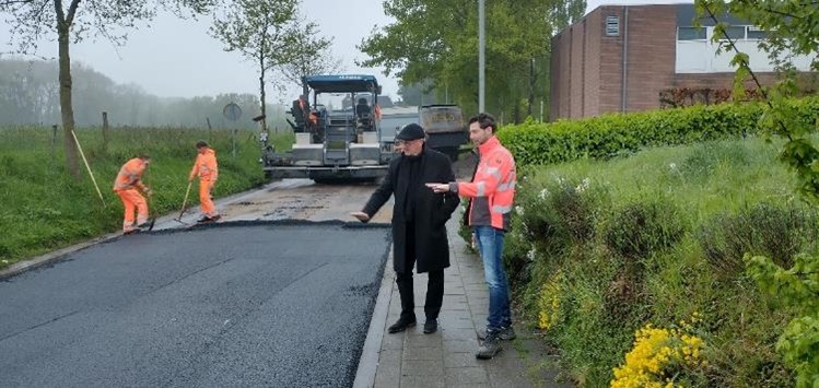 straat half geasfalteerd met uitvoerders en wals. Medewerker Bas Houben van de gemeente legt aan wethouder Jan Weling uit wat de werkzaamheden zijn.